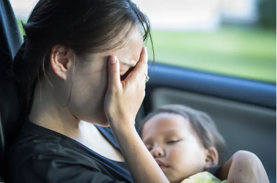 mom in a car face-palming while holding a sleeping baby