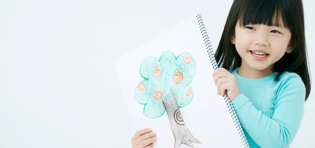 girl holding a drawing of an apple tree with fruits