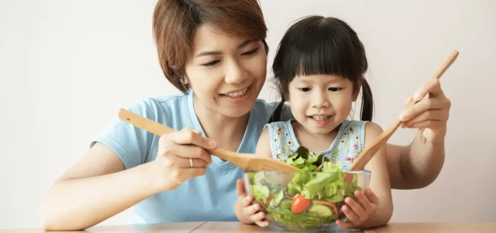 mom and daughter mixing a bowl of salad together